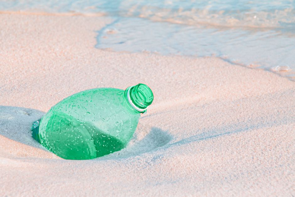Botella de plástico desechada en la playa de arena que ilustra la contaminación ambiental.