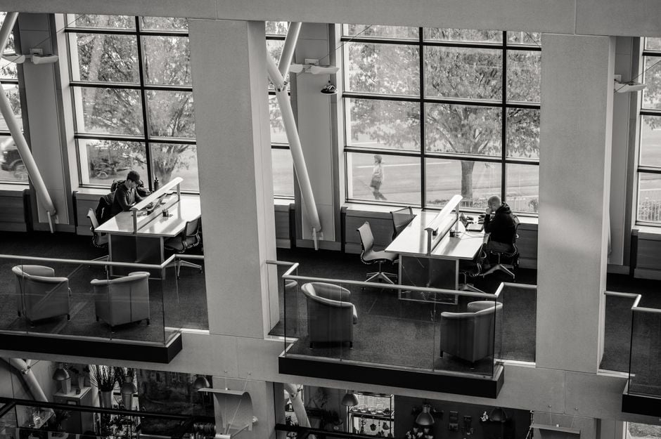 Foto en blanco y negro de una biblioteca moderna de dos plantas con usuarios sentados en escritorios.