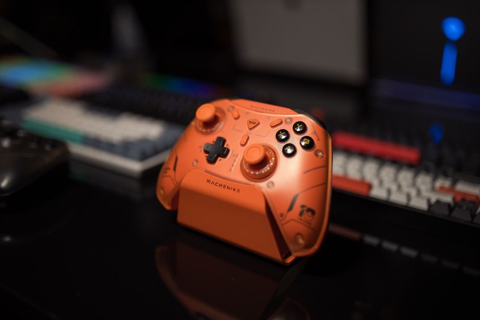 Primer plano de un controlador de juego de color naranja vibrante sobre un escritorio con un teclado en el fondo.