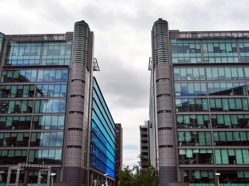 Paisaje urbano que presenta rascacielos modernos con fachada de vidrio reflectante bajo un cielo nublado.