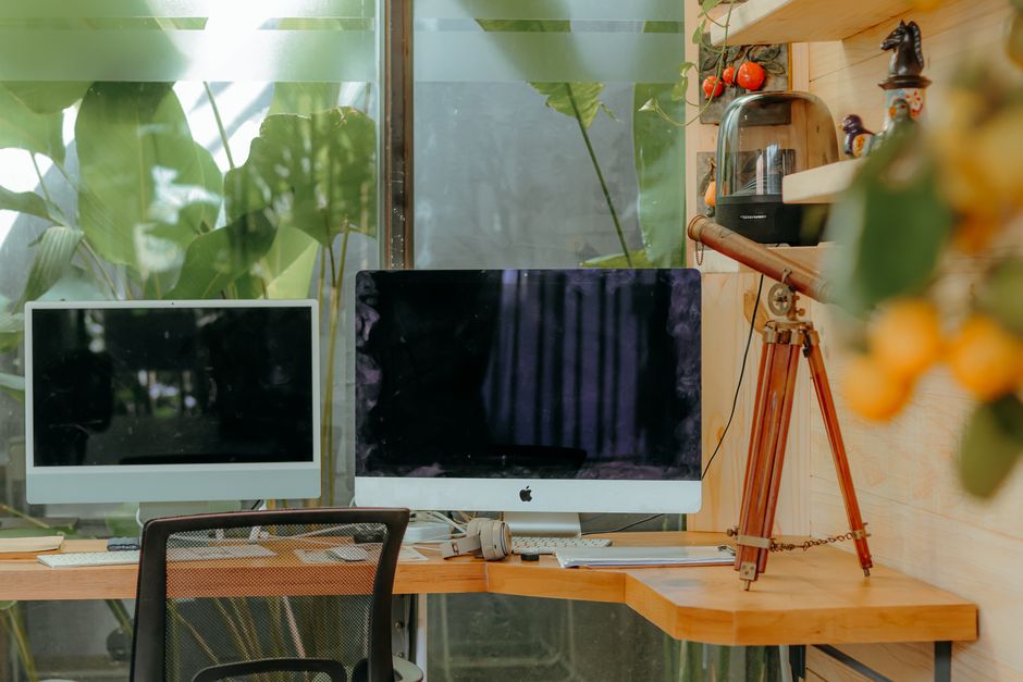Espacio de trabajo contemporáneo con monitores duales, telescopio y plantas que mejoran un ambiente fresco y creativo.