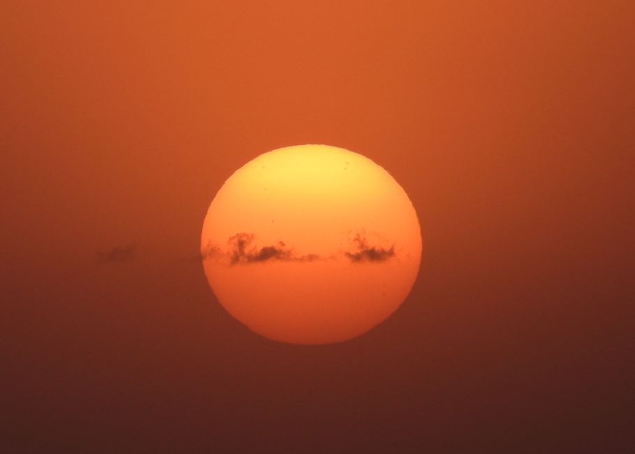 Un primer plano impresionante del sol con nubes dramáticas en un cálido cielo naranja.