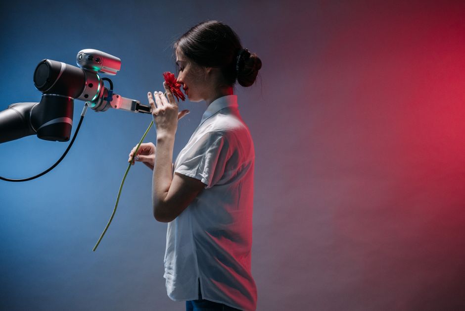 Una mujer con bata de laboratorio interactúa con un brazo robótico que sostiene una flor roja, simbolizando la tecnología y la naturaleza.