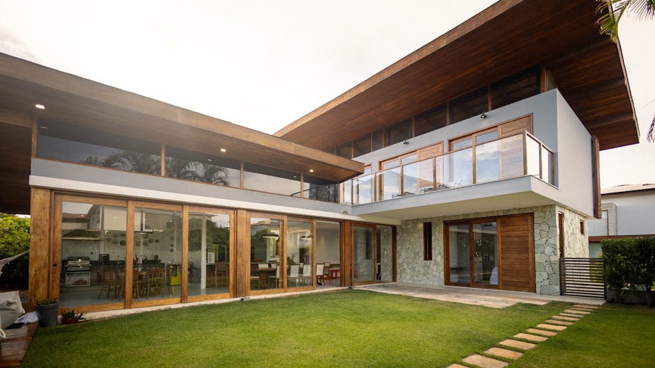 Exterior de casa de lujo contemporánea con grandes ventanales, decoración de madera y césped verde.