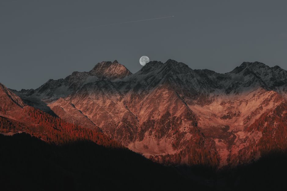 Impresionante vista de las cumbres montañosas bajo la luz de la luna con un resplandor crepuscular que crea un paisaje dramático.