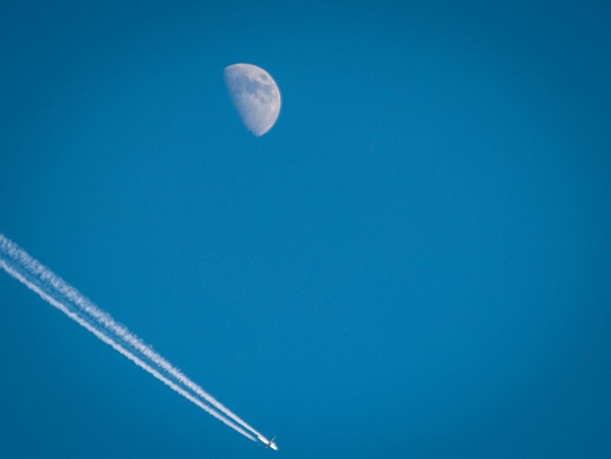 Una impresionante captura de un avión volando bajo una media luna contra un cielo azul vibrante.
