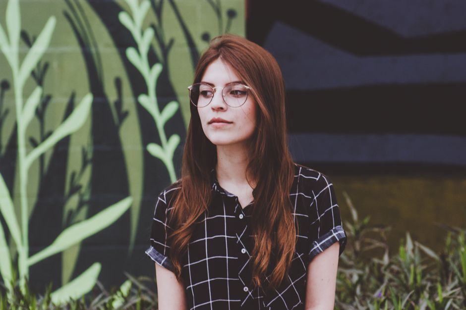 Retrato de una joven con gafas de pie al aire libre contra un fondo de mural.