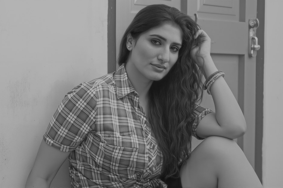 Retrato en blanco y negro de una mujer sentada en un interior, vistiendo una camisa a cuadros y con una expresión segura.