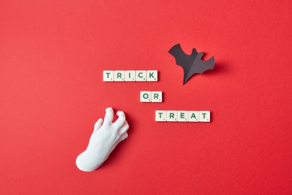 Composición conceptual de Halloween con 'truco o trato' en fichas de scrabble sobre un fondo rojo.