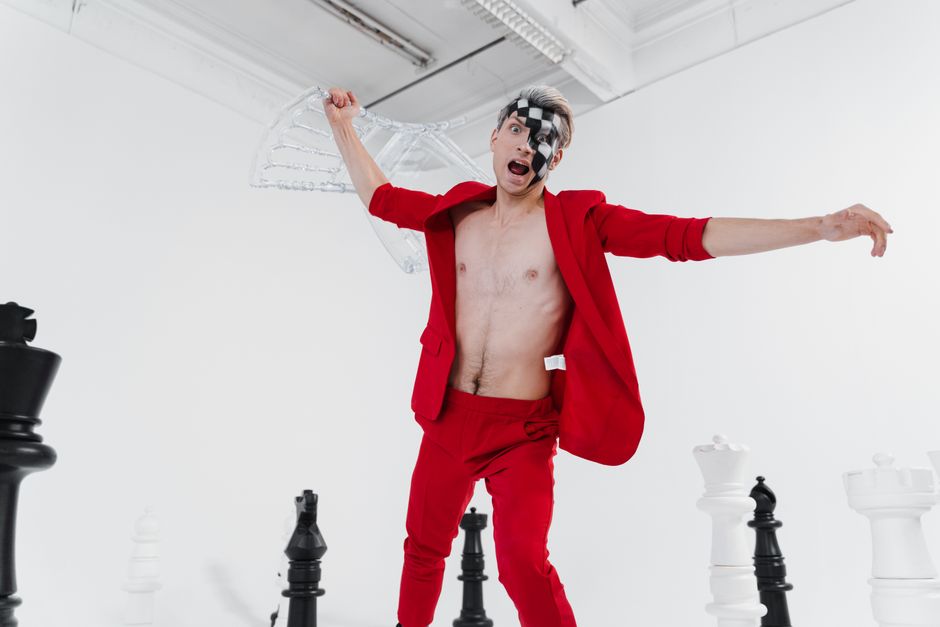 Imagen dinámica de un hombre sin camiseta en un traje rojo con pintura facial expresando creatividad en un entorno inspirado en el ajedrez.