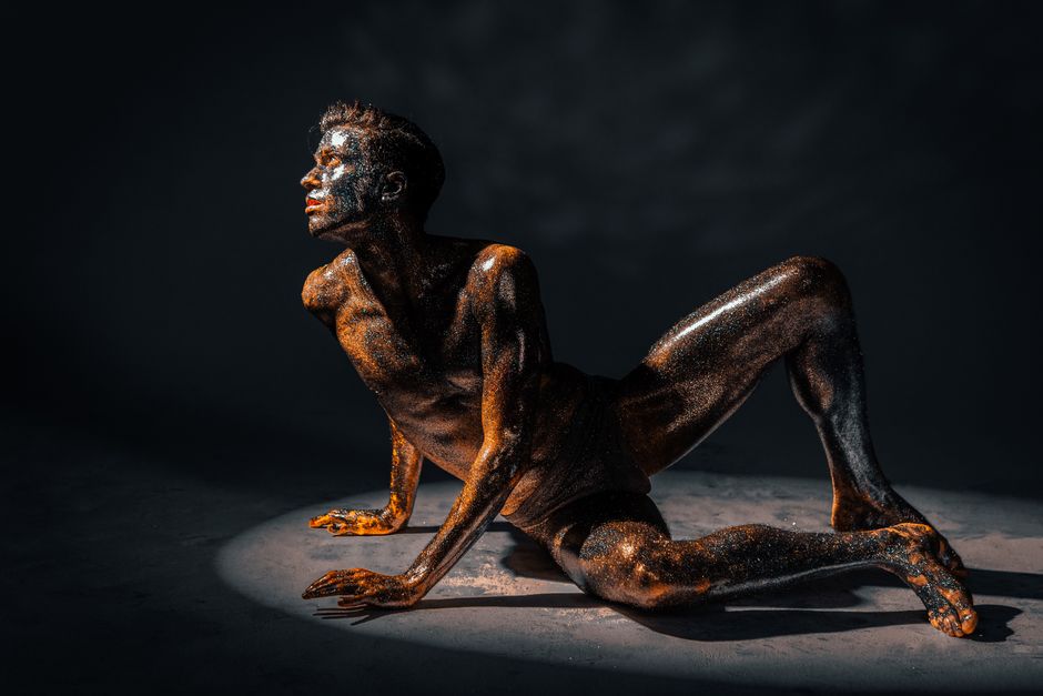 Un modelo masculino sin camisa posando con purpurina en una fotografía de estudio dramática y artística.