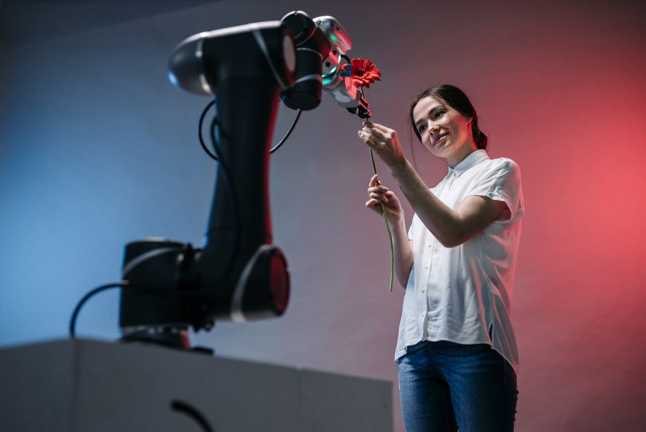 Una mujer y un brazo robótico sosteniendo una flor de manera colaborativa, simbolizando el toque suave de la tecnología.