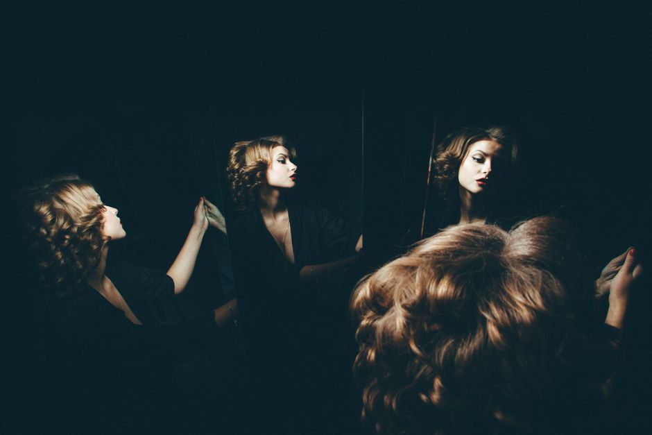 Retrato artístico de una mujer reflejada en espejos, mostrando una iluminación y sombras dramáticas.