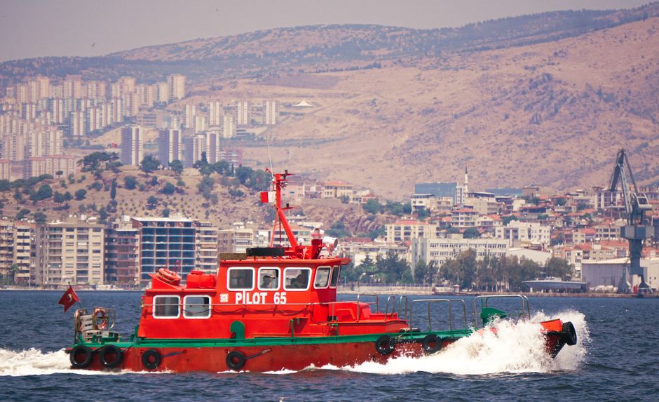 Un colorido barco piloto navega en la bahía de Esmirna con un paisaje urbano de fondo en Turquía.