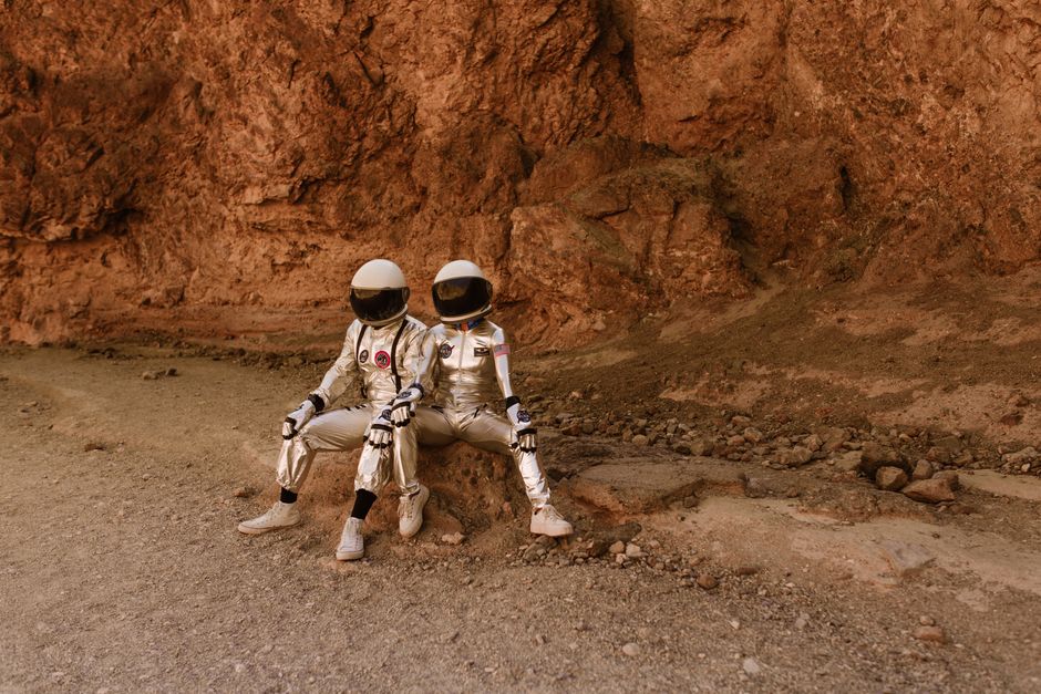 Dos astronautas en trajes espaciales se relajan en un terreno rocoso que recuerda a Marte, evocando exploración y aventura.