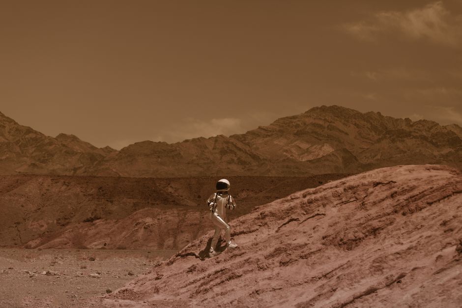 Astronauta caminando en un paisaje árido que se asemeja a Marte, con vibraciones futuristas y aventureras.