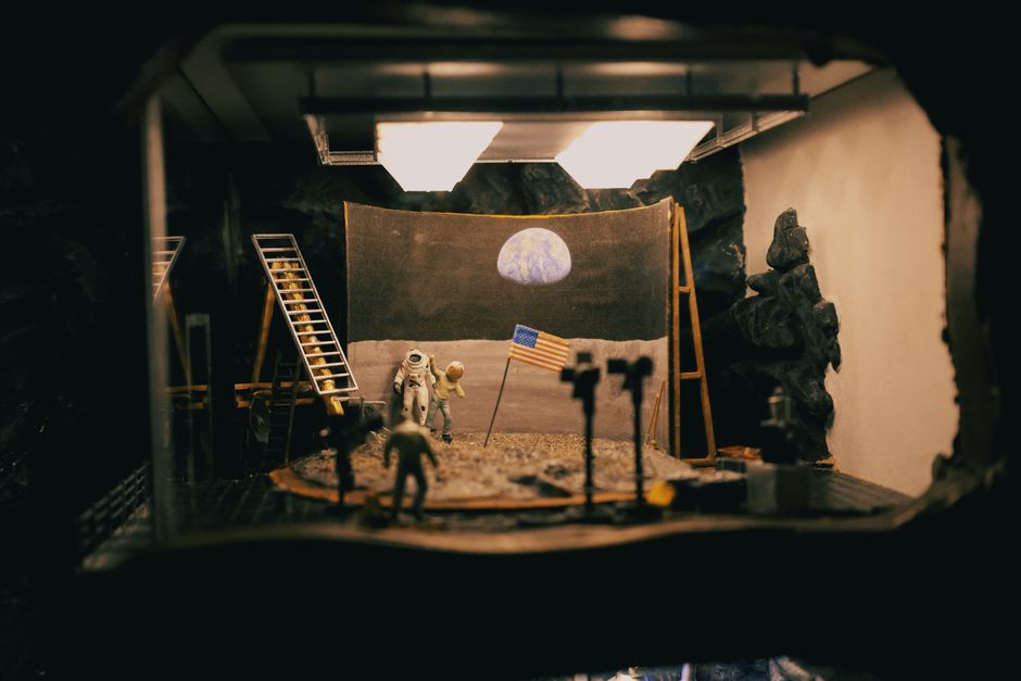 Un diorama creativo que representa el alunizaje con astronautas y bandera en un entorno de estudio.