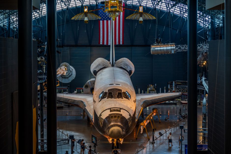 El transbordador espacial expuesto en un museo con la bandera estadounidense visible al fondo.