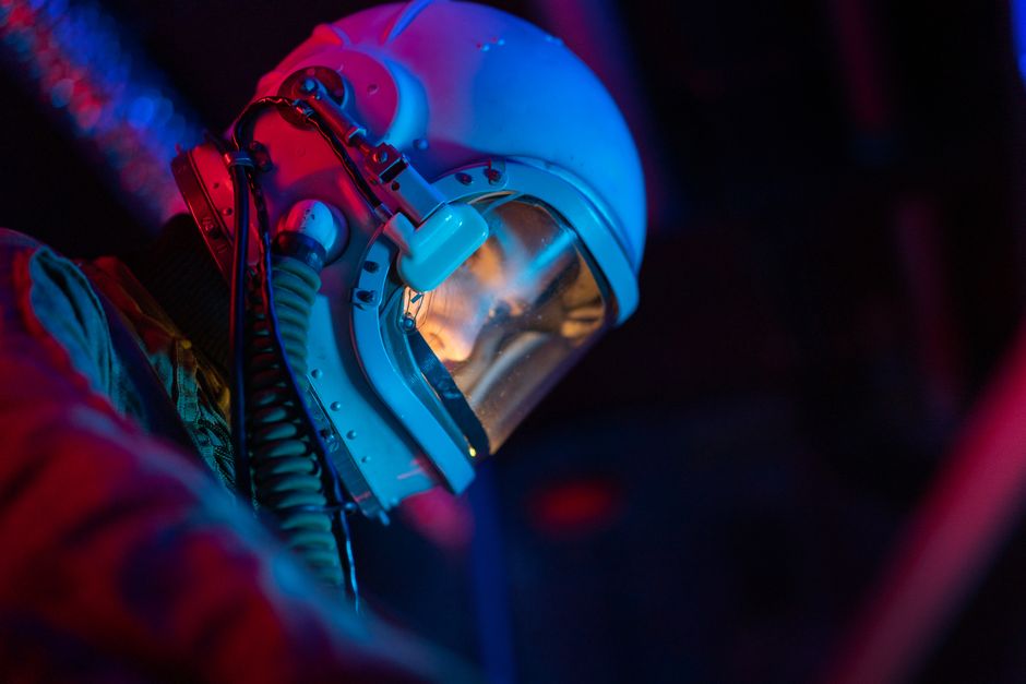 Una astronauta en un traje de alta tecnología con casco iluminado frente a un fondo oscuro y futurista.