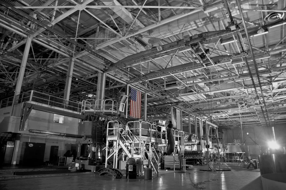 Foto en blanco y negro de una amplia instalación industrial con la bandera americana colgando de manera prominente.
