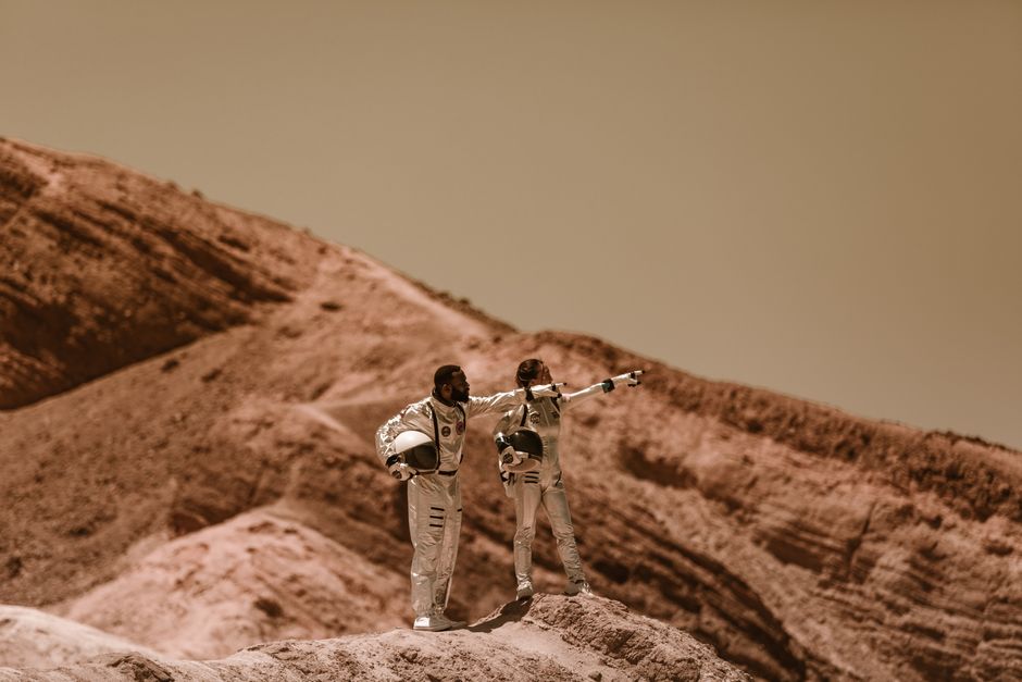 Dos astronautas en trajes espaciales exploran un paisaje árido, similar al de Marte.