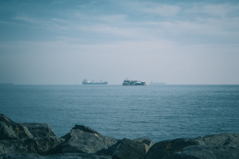 Buques de carga navegando en un mar en calma bajo un cielo nublado, vista del horizonte.