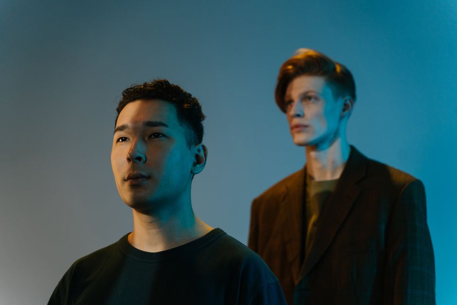 Retrato de dos hombres en un estudio con iluminación artística azul y naranja, mostrando contraste creativo.