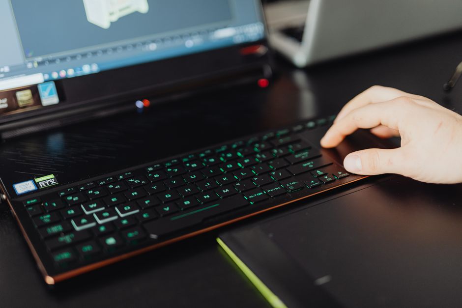 Primer plano de una mano en el teclado de un portátil trabajando en un proyecto de modelado 3D con teclas LED verdes.