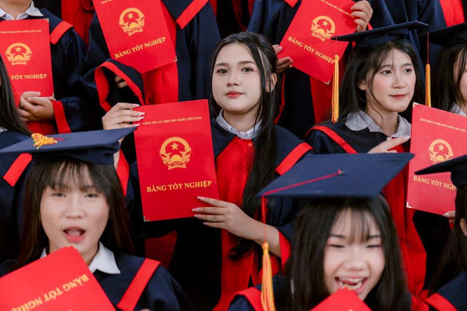 Graduados con toga y birrete sostienen con orgullo sus diplomas vietnamitas en una ceremonia.