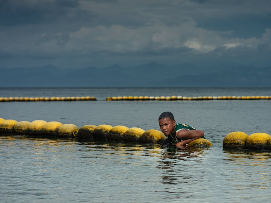 Un adolescente descansa sobre boyas en el océano bajo un cielo dramático, creando un contraste atractivo.