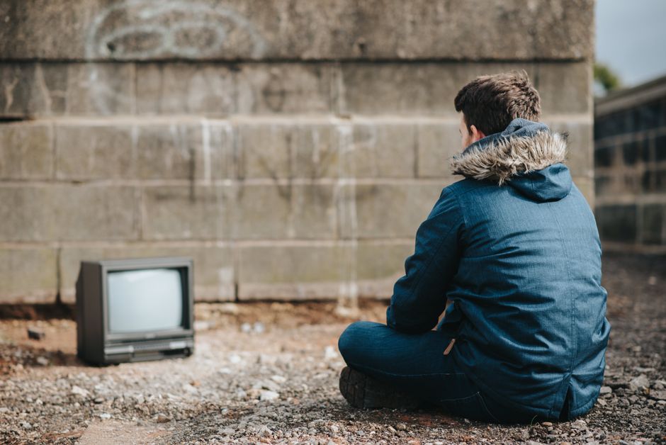 Un hombre con una chaqueta azul está sentado al aire libre frente a un televisor vintage, destacando la nostalgia retro.