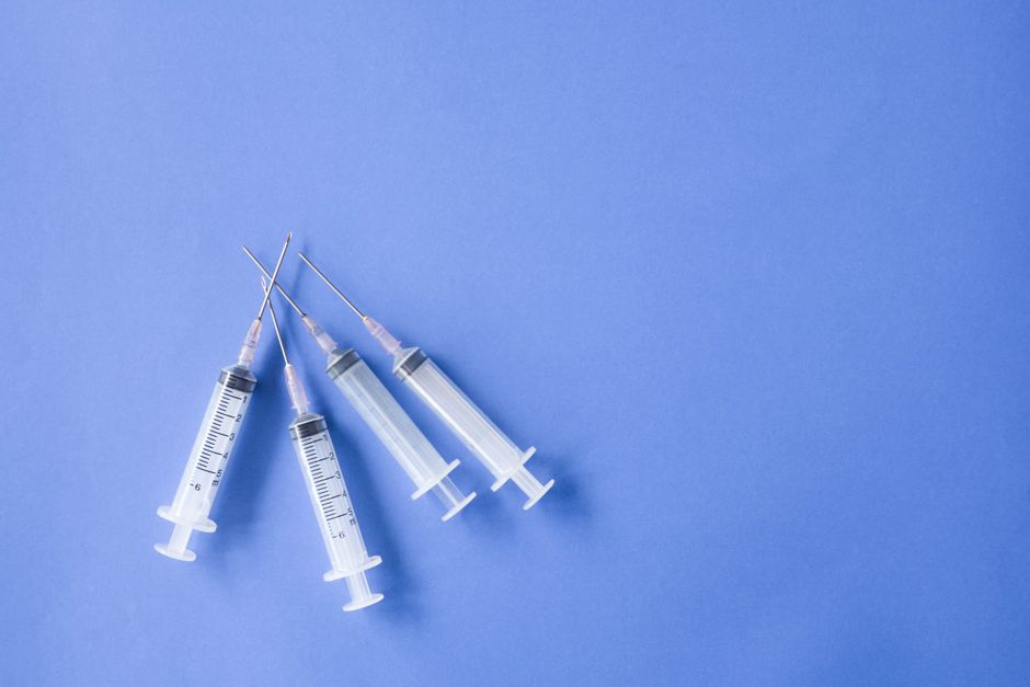 Cuatro jeringas médicas dispuestas sobre un fondo azul, ideal para temas de salud.