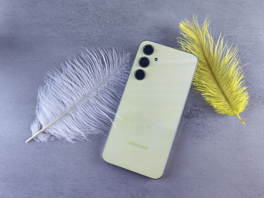 Disposición flat lay de un smartphone amarillo con plumas sobre un fondo gris, perfecto para temas de tecnología y estilo de vida.