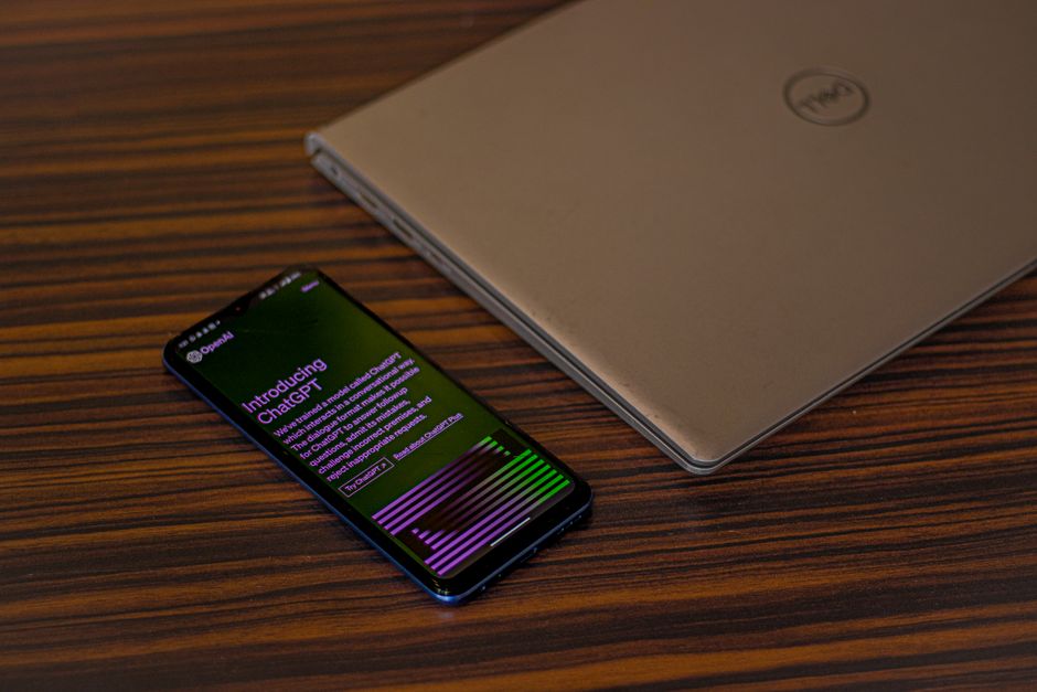 Un smartphone mostrando la aplicación ChatGPT junto a un portátil cerrado sobre una mesa de madera.