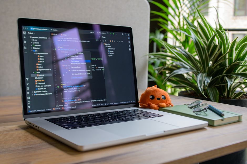 Portátil con interfaz de codificación, planta y juguete para un ambiente de trabajo acogedor.