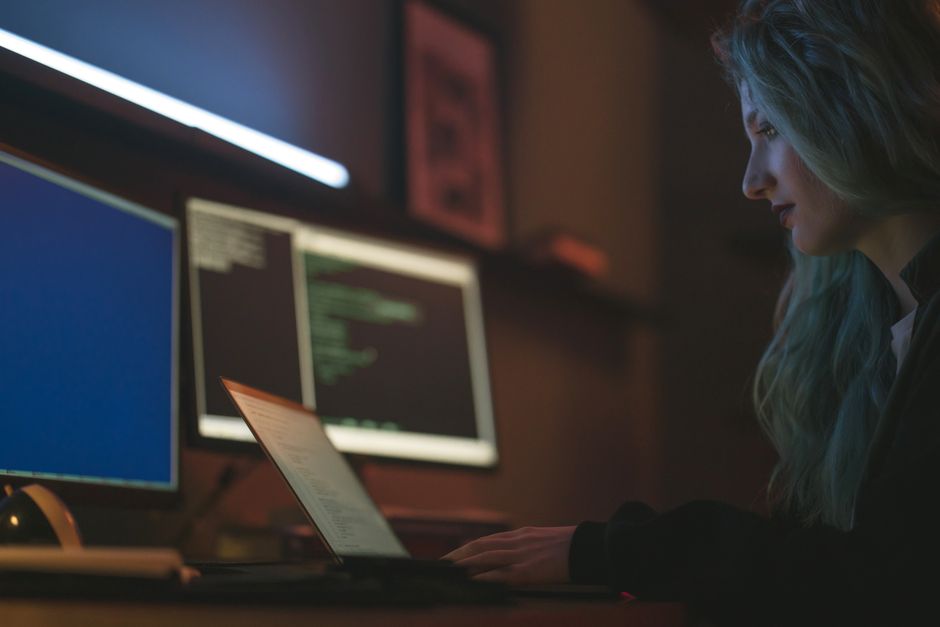 Mujer trabajando en programación de ciberseguridad con portátiles y múltiples pantallas