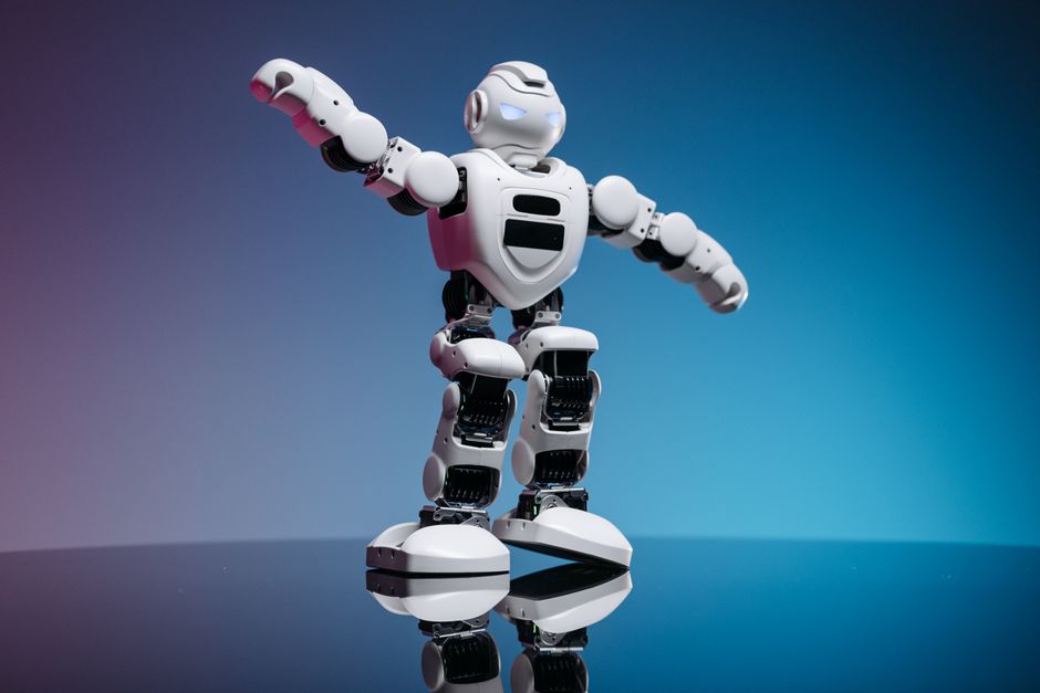 Un juguete robot blanco futurista de pie sobre una superficie reflectante con un fondo degradado.