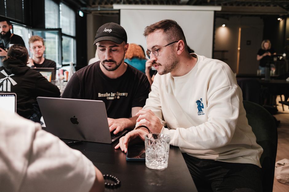 Dos hombres colaborando en un proyecto en un café moderno con portátiles y gafas.