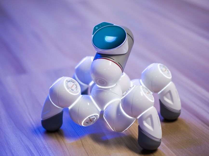 Un juguete robótico elegante y blanco sobre un suelo de madera con un fondo borroso y luz azul.