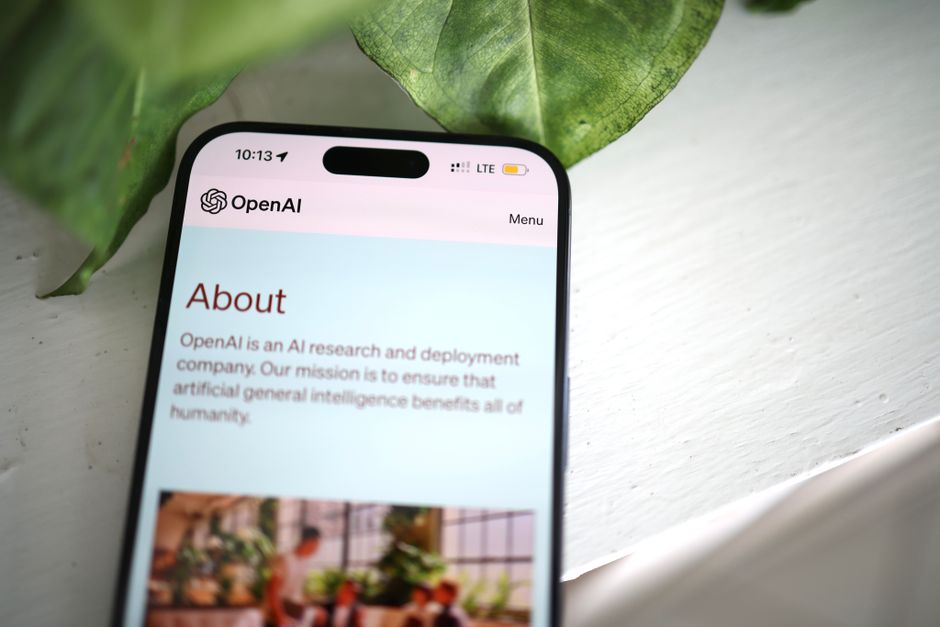 Disparo en primer plano de la pantalla de un smartphone mostrando el sitio web de OpenAI con vegetación de fondo.