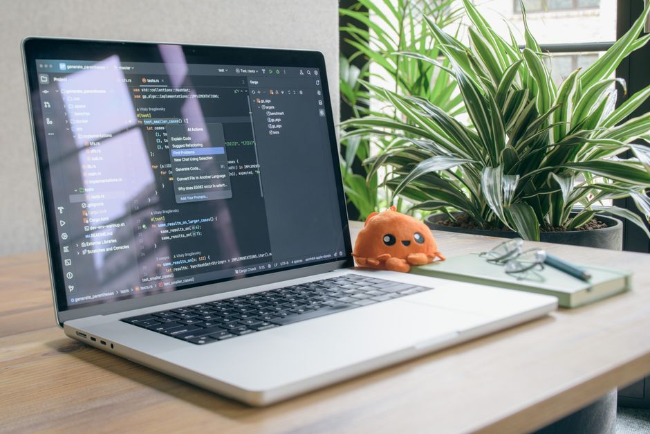 Un espacio de oficina en casa moderno con un ordenador portátil con software de programación, una planta y un peluche.