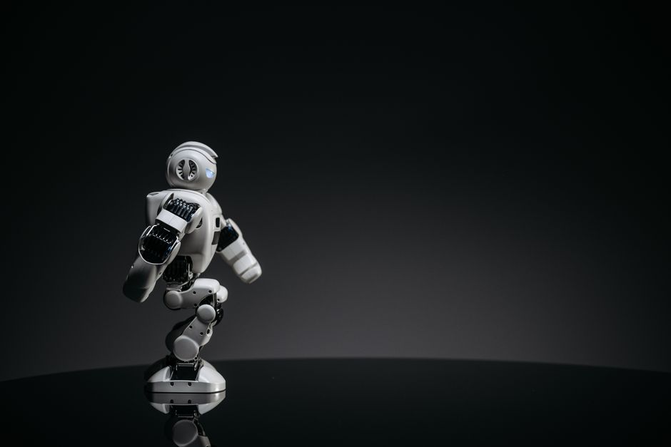 Un elegante robot de juguete blanco posado con gracia contra un fondo oscuro de estudio.