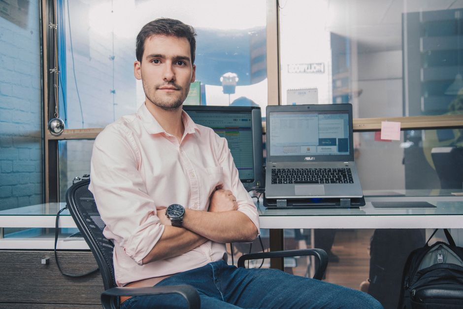 Joven profesional masculino con una actitud segura sentado en un escritorio moderno con una laptop.