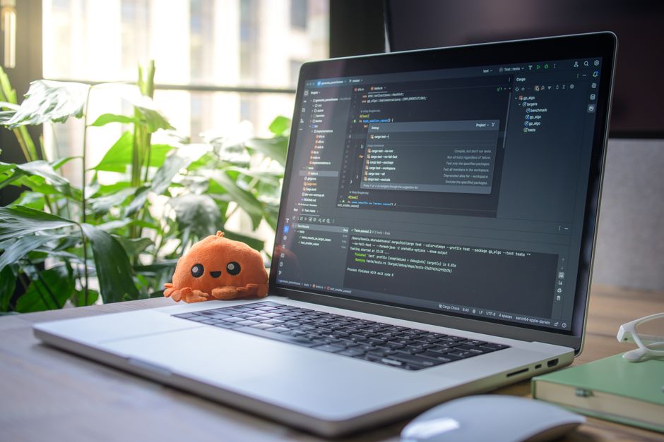 Portátil sobre el escritorio con IDE abierta, mostrando el entorno de codificación, junto a un juguete de peluche y plantas.