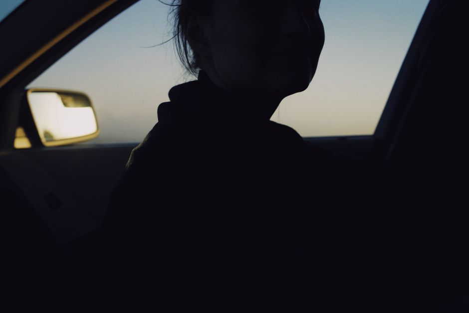 Una silueta misteriosa de una mujer dentro de un coche al atardecer, con un enfoque en sombras y luz.