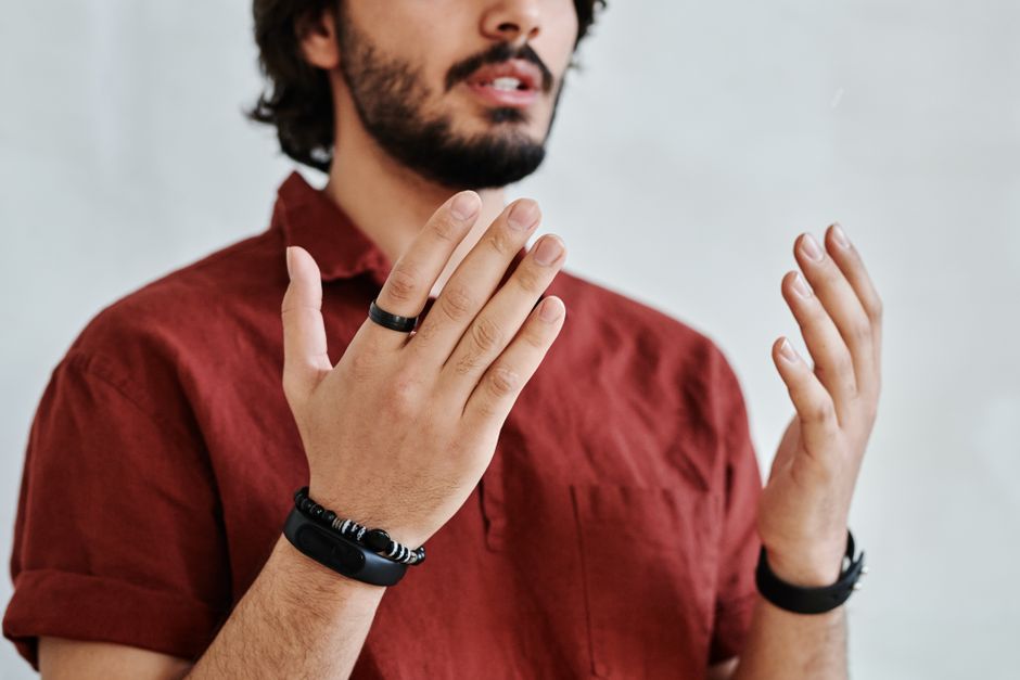 Primer plano de las manos de un hombre con pulseras y anillos gesticulando sobre un fondo blanco.
