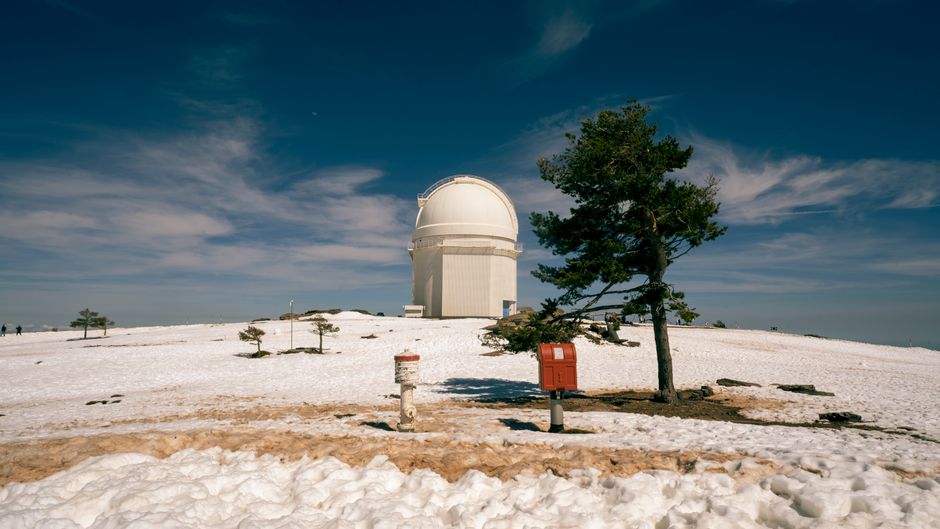 Una vista pintoresca del Observatorio Calar Alto rodeado de nieve y árboles bajo un cielo despejado.