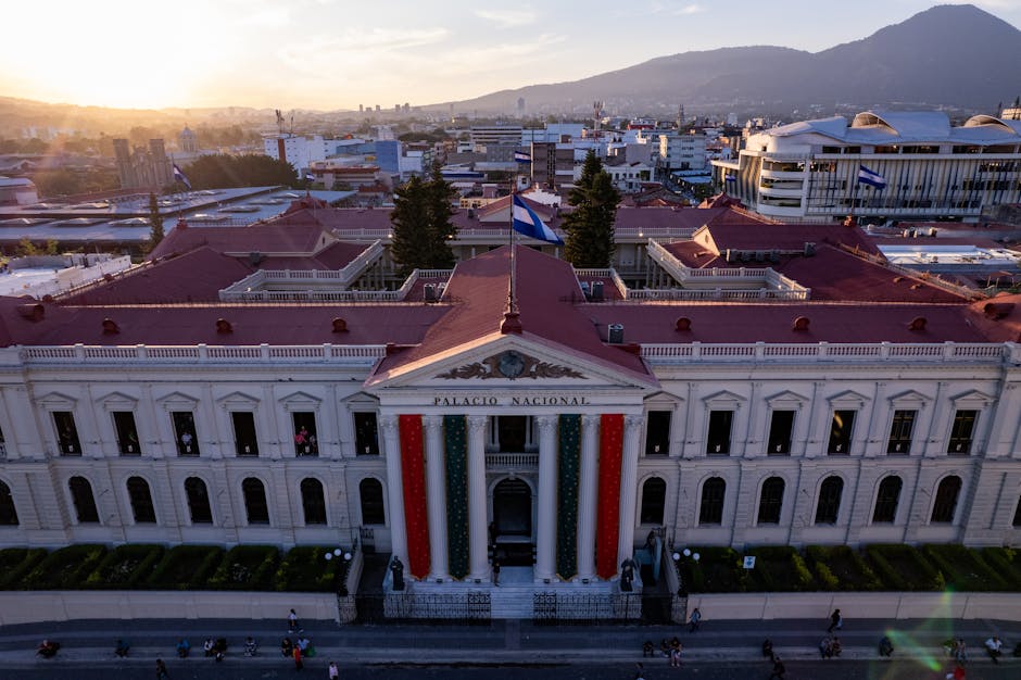 Una cautivadora toma aérea del Palacio Nacional en San Salvador durante el atardecer, que muestra la vibrante vida y arquitectura de la ciudad.