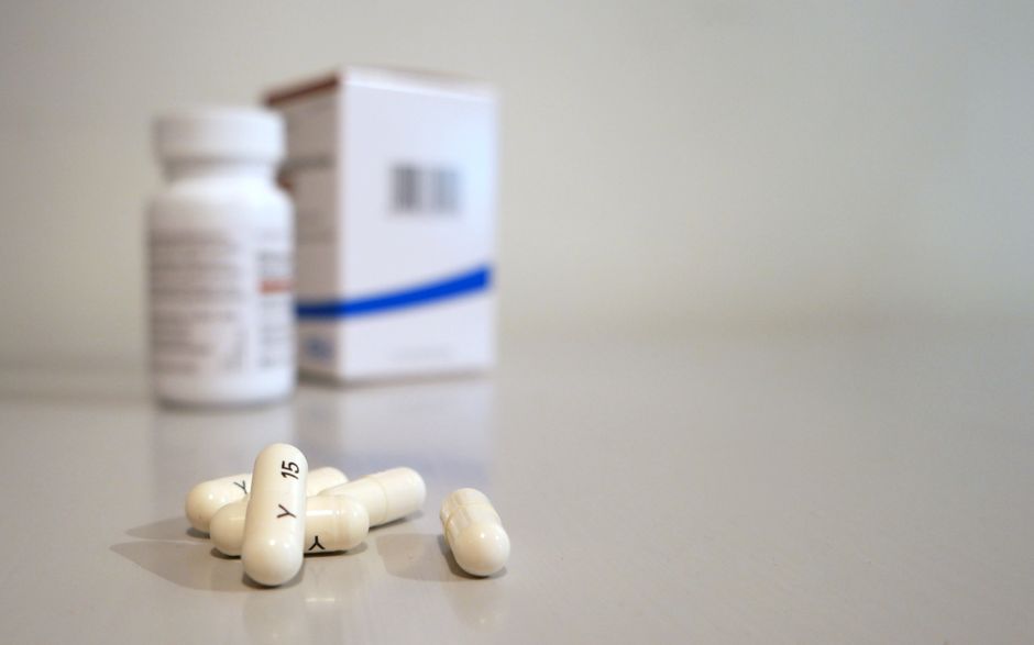 Imagen en primer plano de cápsulas blancas con frasco de medicina y caja al fondo.