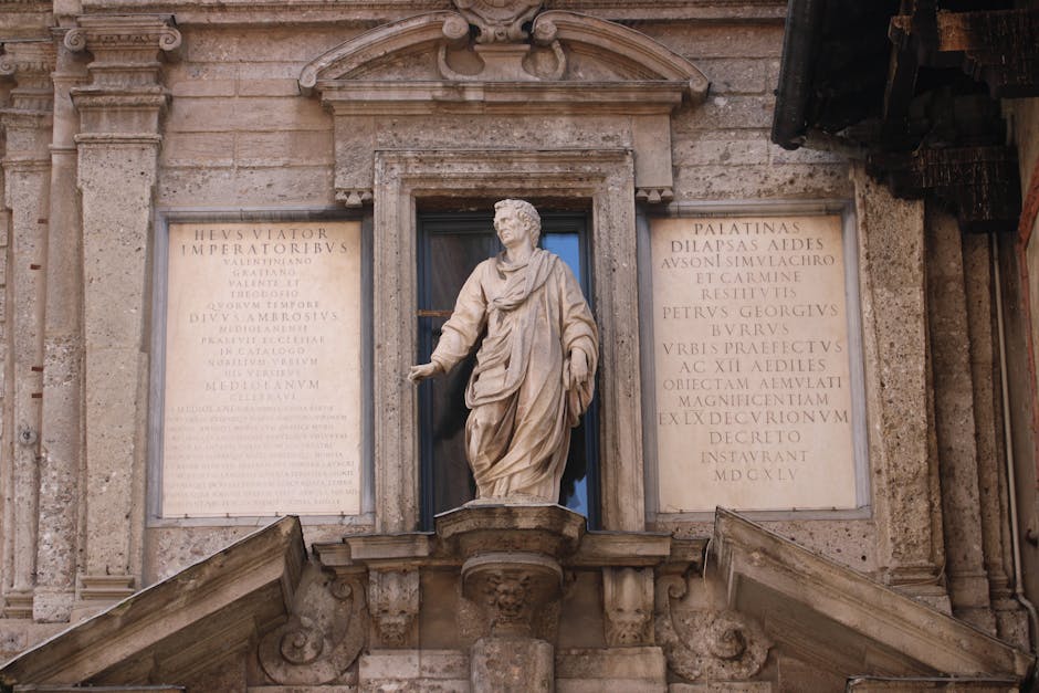 Primer plano de una antigua estatua romana con inscripciones en latín en la fachada de un edificio histórico.